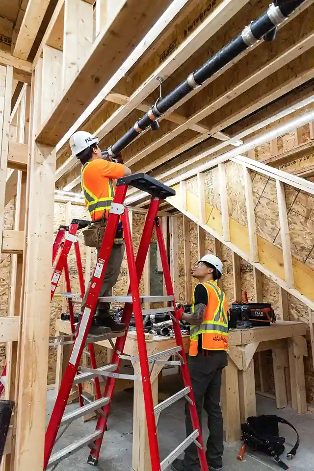 Specialty contractor plumbers installing ceiling drainage pipes on a framed job site